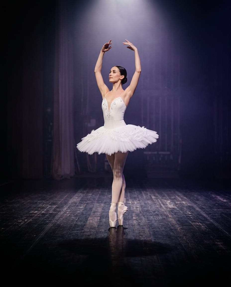 Una bailarina en puntas con tutú blanco bajo un foco